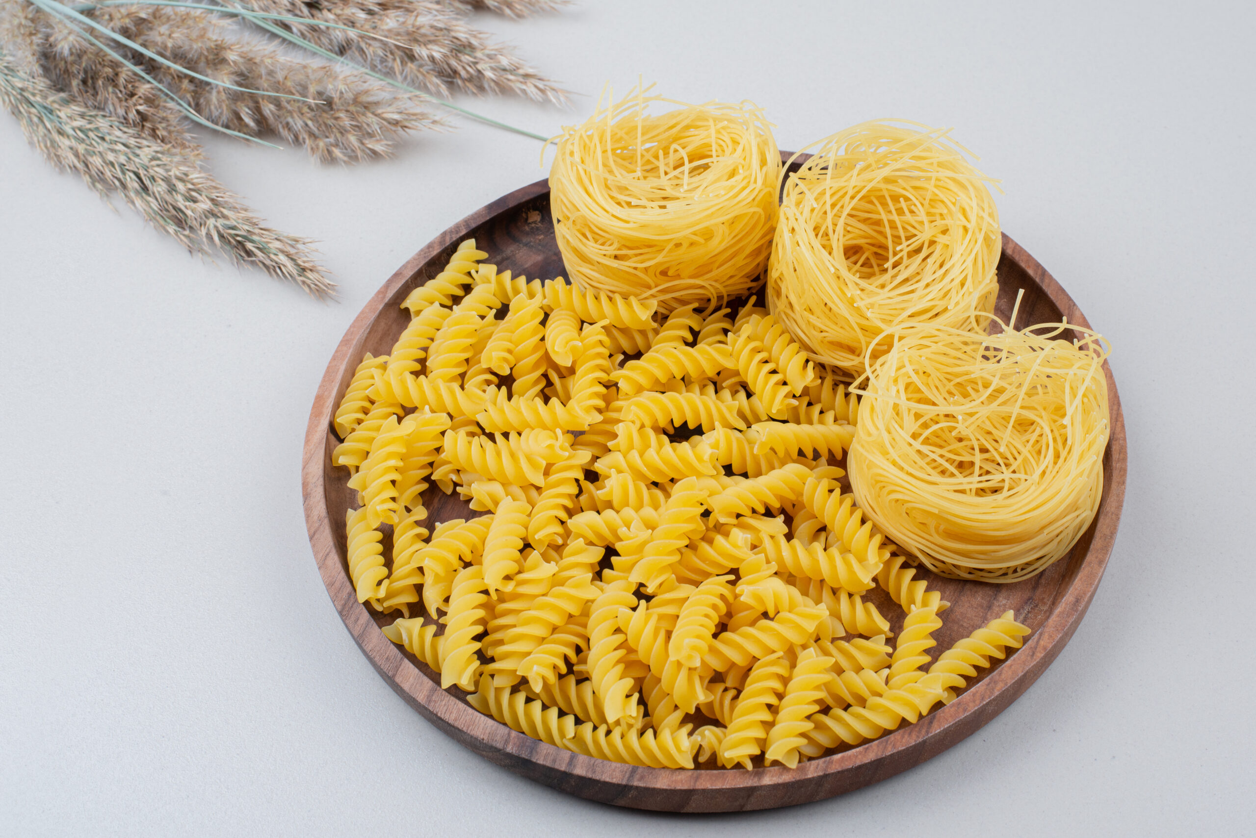 Raw spiral macaroni and spaghetti on wooden plate. High quality photo